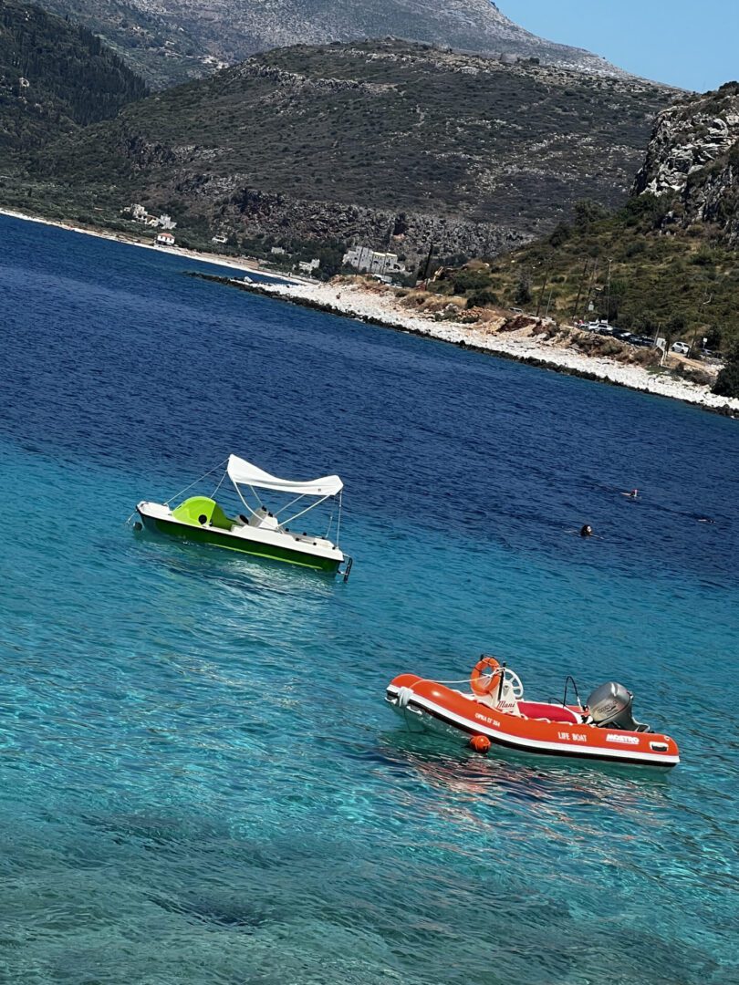 Two pedal boats floating on clear blue water near a rocky shore.
