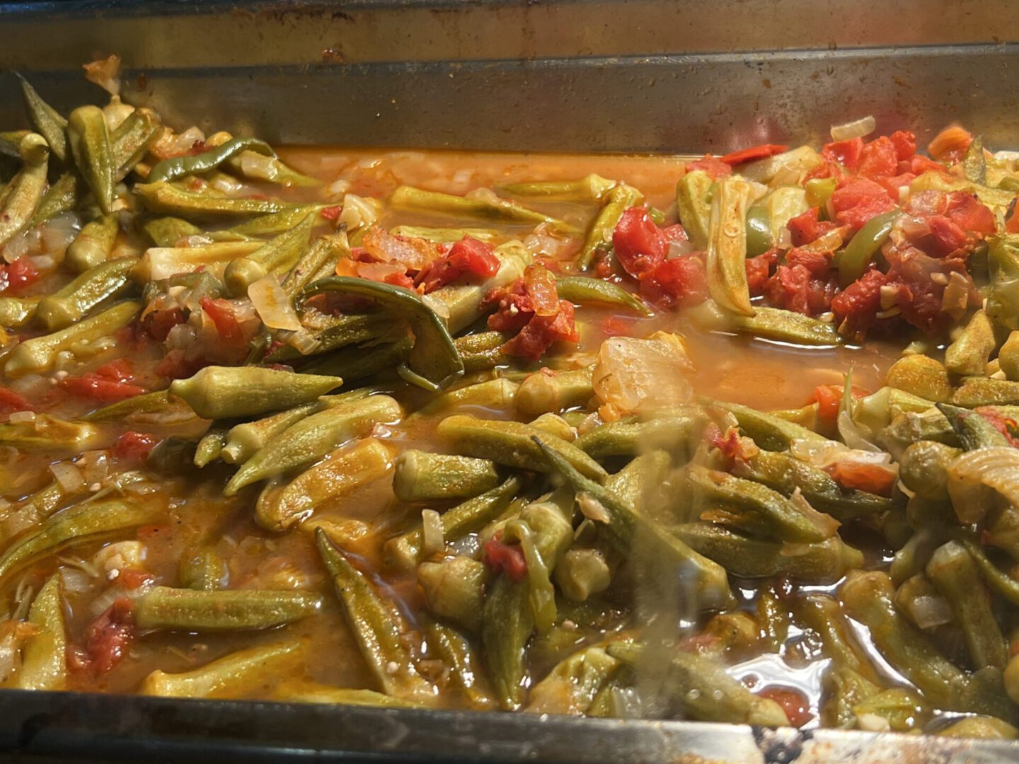A pan of cooked green beans with diced tomatoes and seasoning.