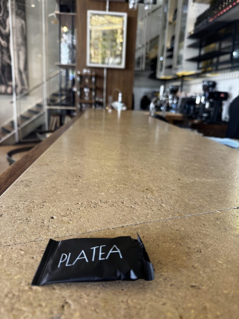 A black wallet labeled 'PLATEA' on a polished countertop in a café.