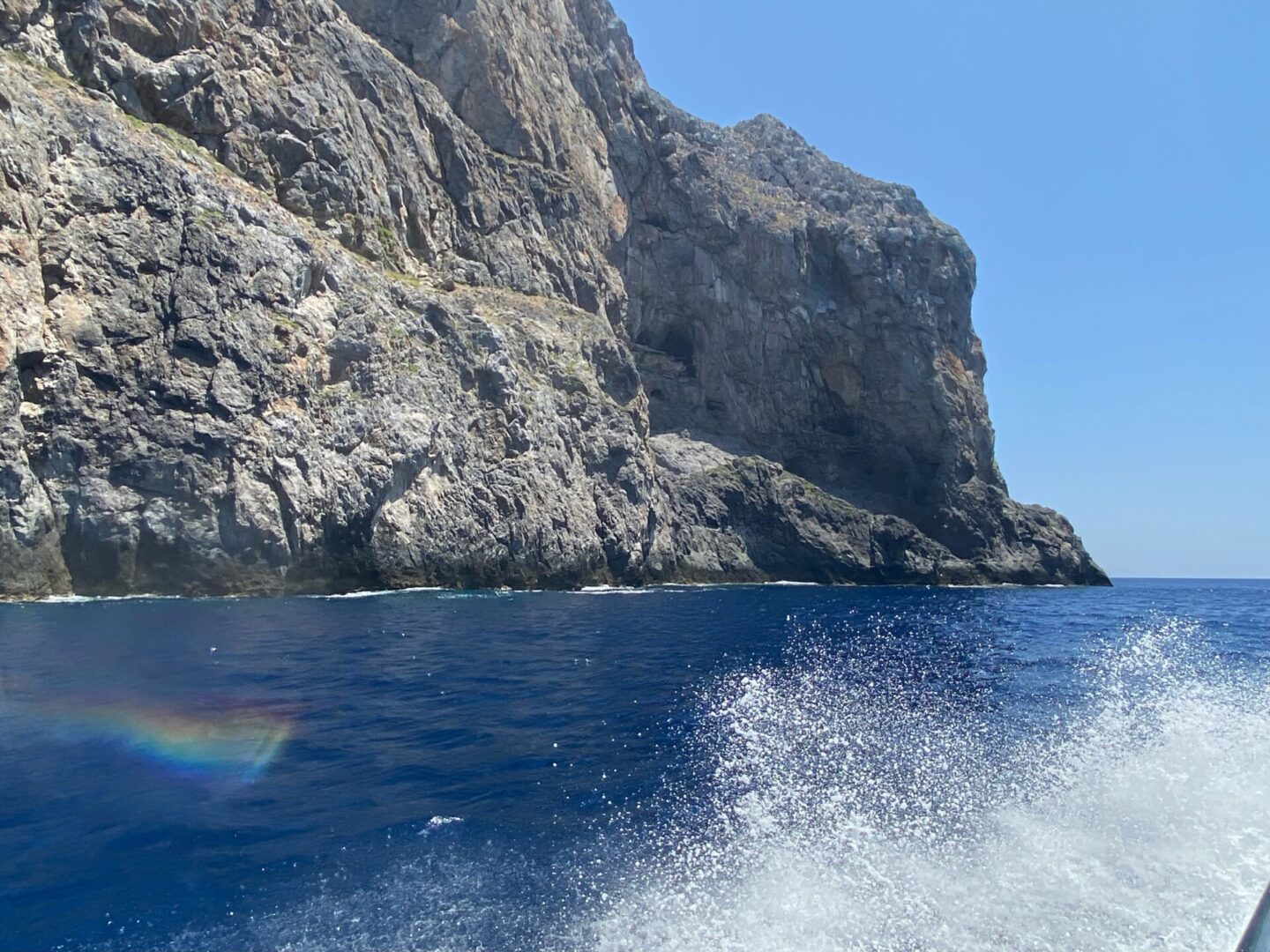 Cliffside view over deep blue sea with boat wake in the foreground.