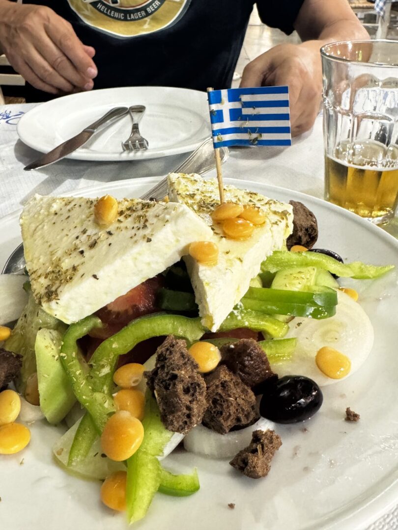 Greek salad with pita, olives, and a small Greek flag on the plate.