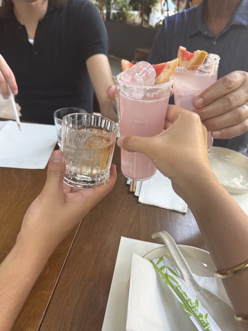 Friends cheers with cocktails at table.