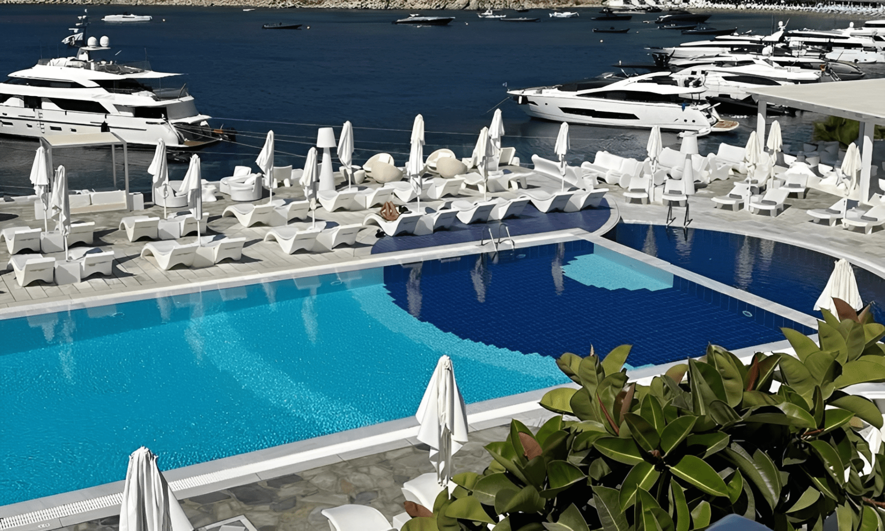 Empty poolside area with white loungers and umbrellas by the sea.