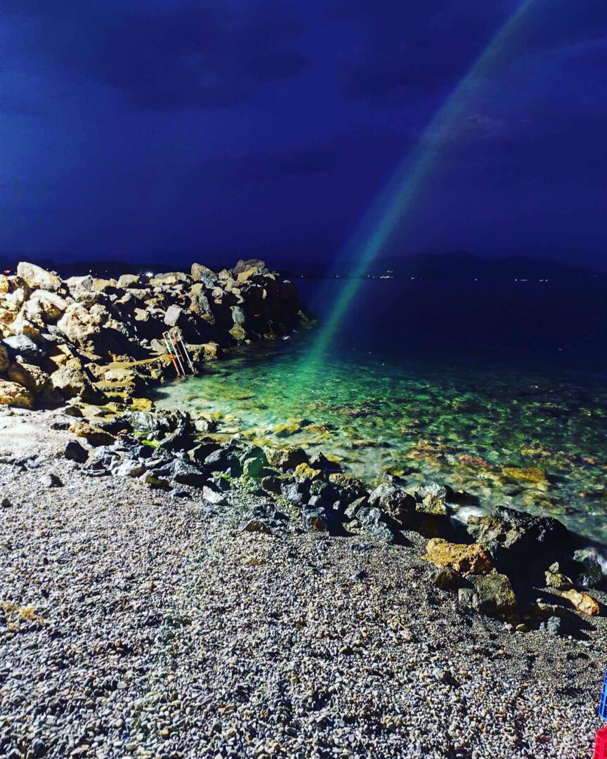 A nighttime beach scene with clear water and a green light beam.