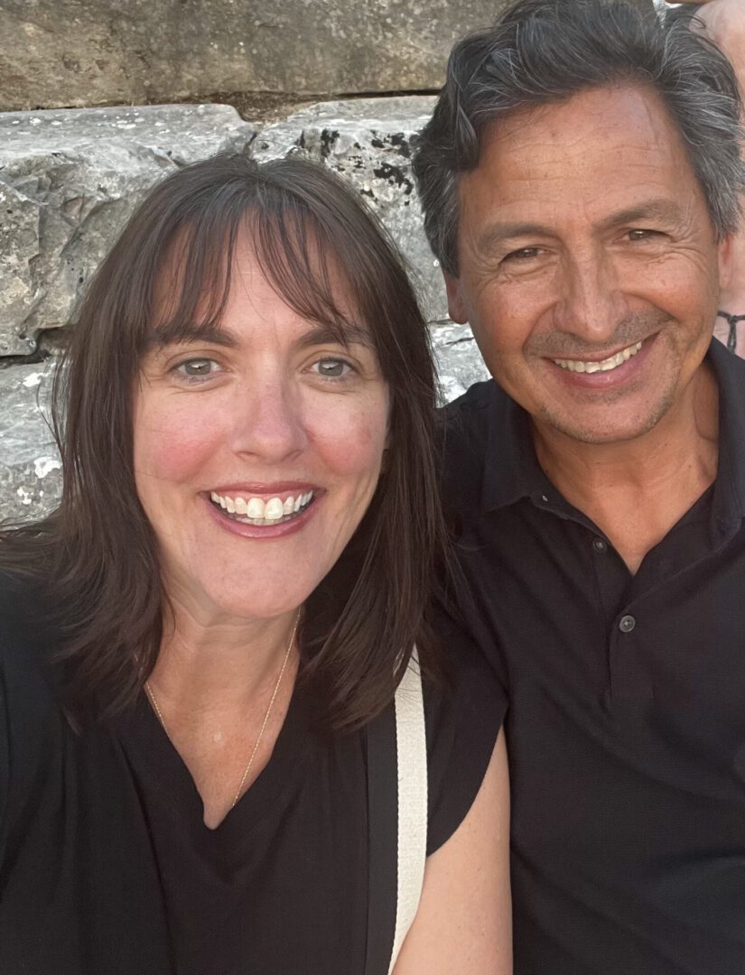Smiling couple posing outdoors with stone wall background.