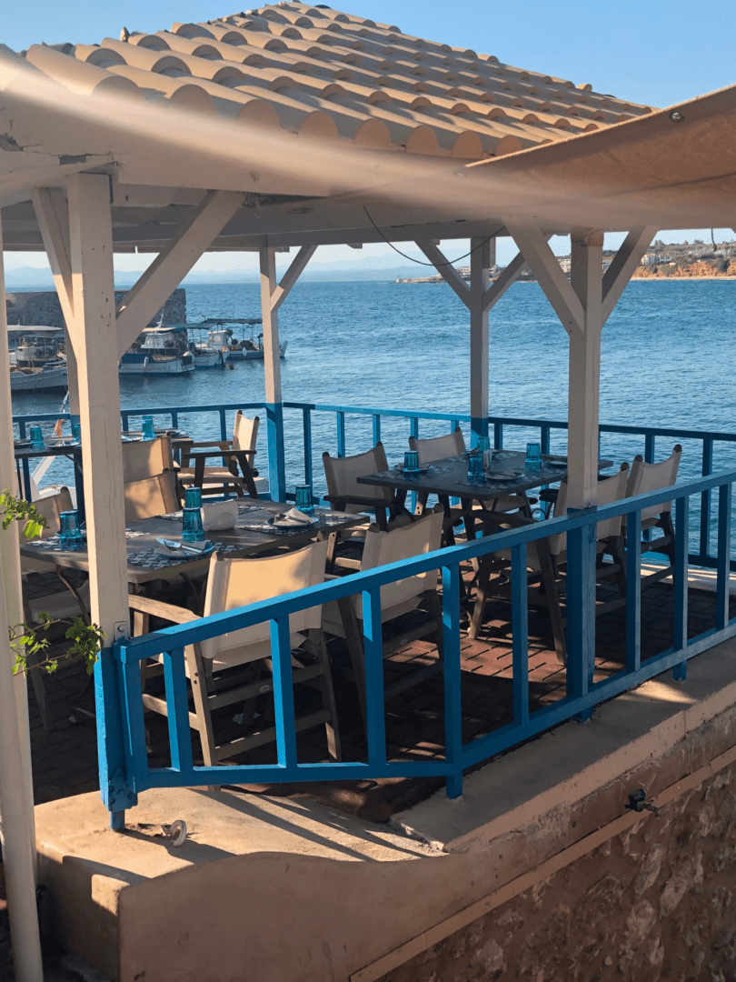 Outdoor seaside dining area with tables and chairs under a canopy.