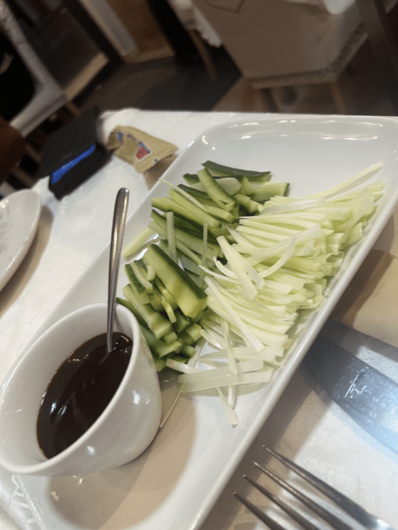 Plate of sliced cucumbers and onions with a dipping sauce and spoon.