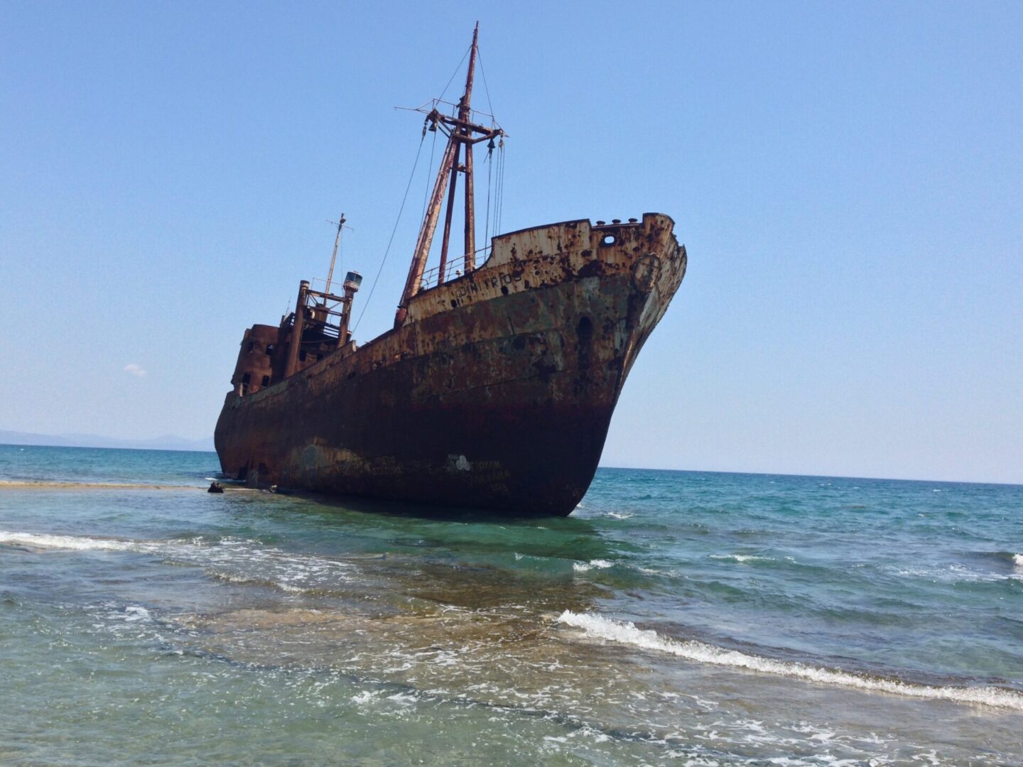 Rusty shipwreck stranded near the shoreline under clear blue sky.