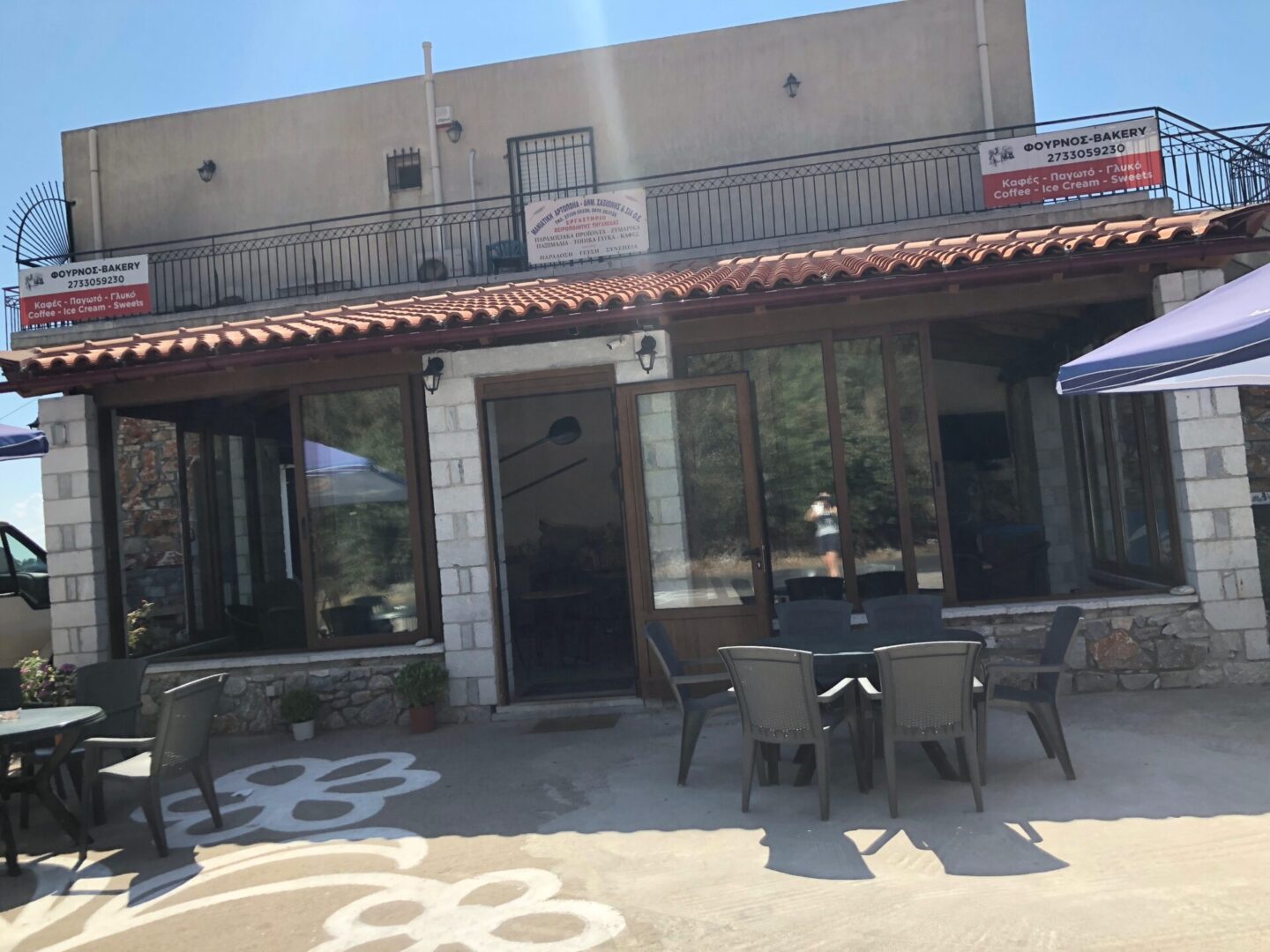 Outdoor seating area in front of a building with glass windows and a tiled roof.