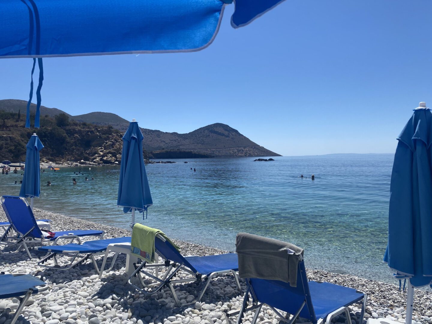 A peaceful beach scene with chairs and an umbrella by clear water.