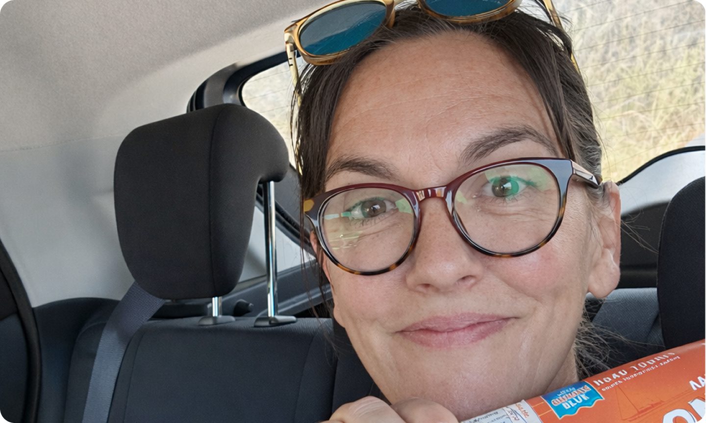 Smiling woman with glasses inside a car, wearing sunglasses on her head.